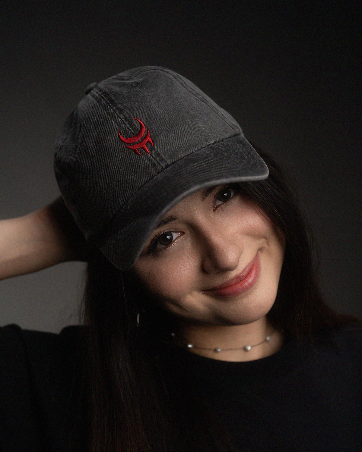 Schwarze, verwaschene Cap mit roter Sichelmond-Stickerei auf der Vorderseite, frontal getragen von einer Person mit langen dunklen Haaren.