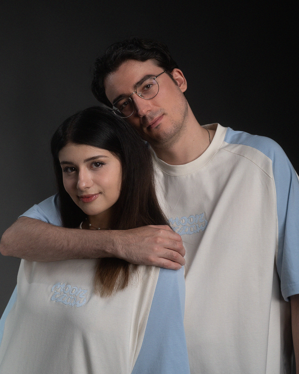 T-Shirt in Off-White mit hellblauen Raglanärmeln, auf der Vorderseite mittig bestickt mit dem Wort „moonclaw“ in geschwungener, hellblauer Schrift. Das Shirt hat einen lockeren, verlängerten Schnitt.