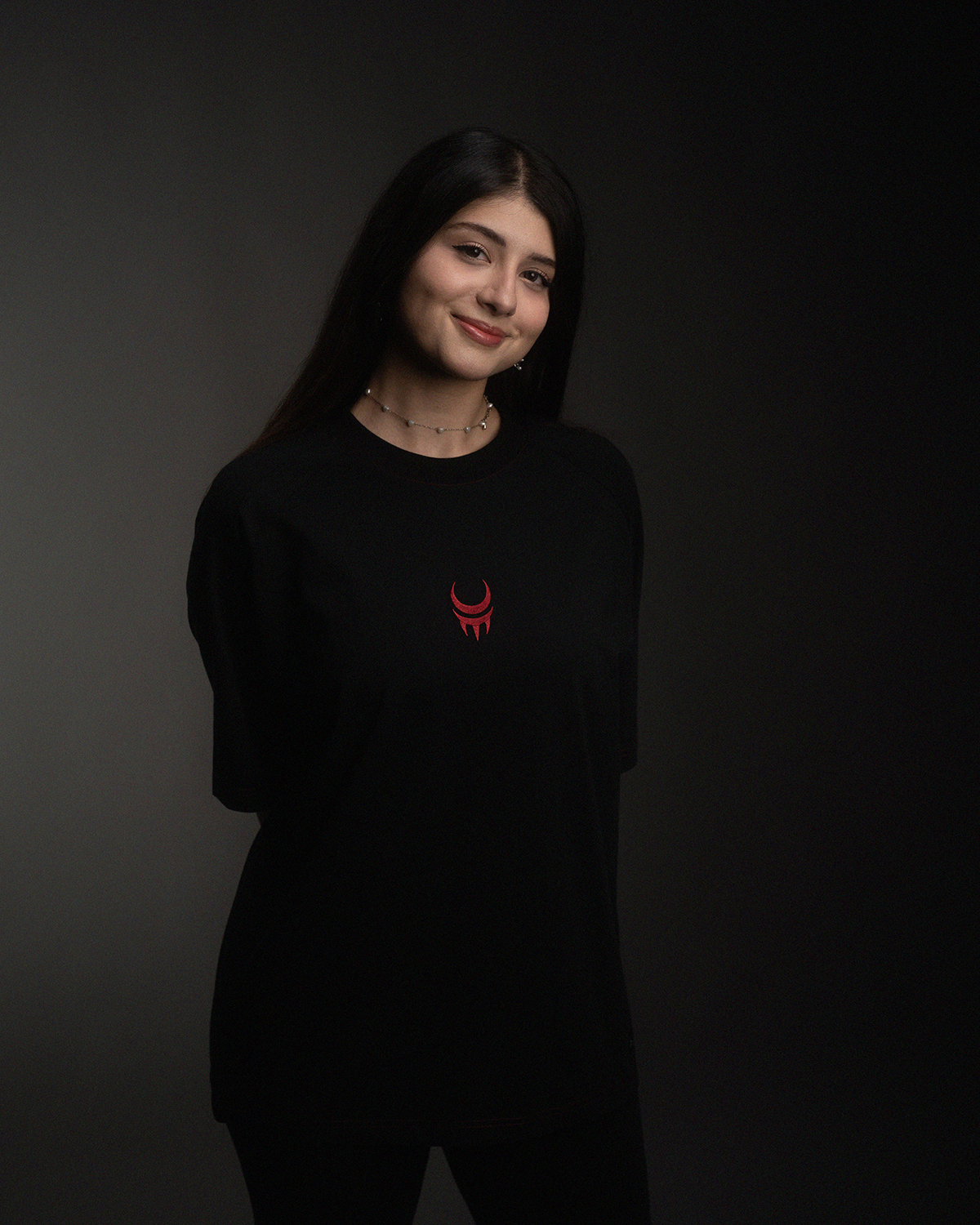 Frau in schwarzem T-Shirt mit rotem Mondkrallen-Logo, lächelt leicht.