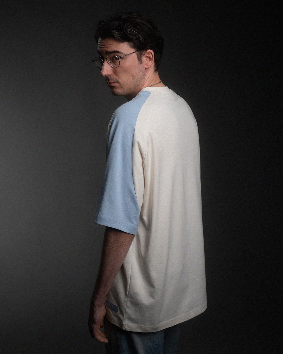 Rückansicht des T-Shirts in Off-White mit hellblauen Raglanärmeln. Der Rücken ist schlicht ohne Aufdruck oder Stickerei.