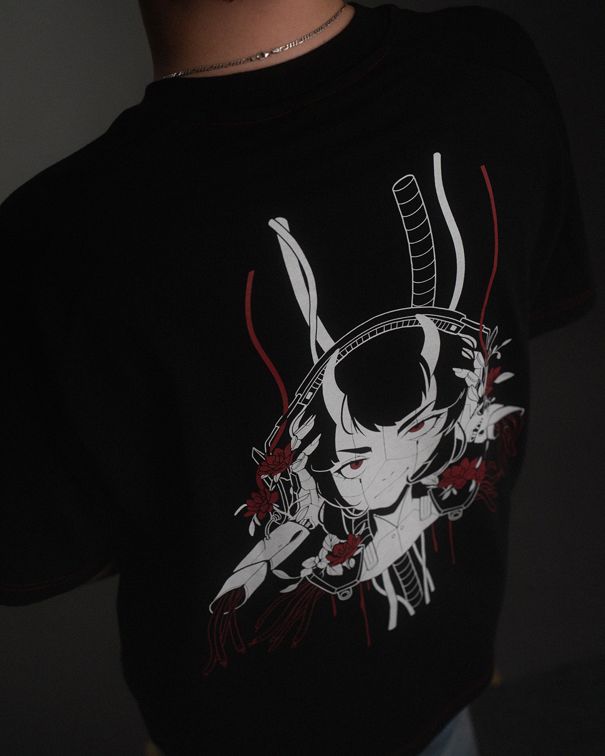 Rückansicht eines schwarzen T-Shirts mit großem Rückendruck: eine gezeichnete Cyborg-Figur mit roten Akzenten, Blumen und Schläuchen.