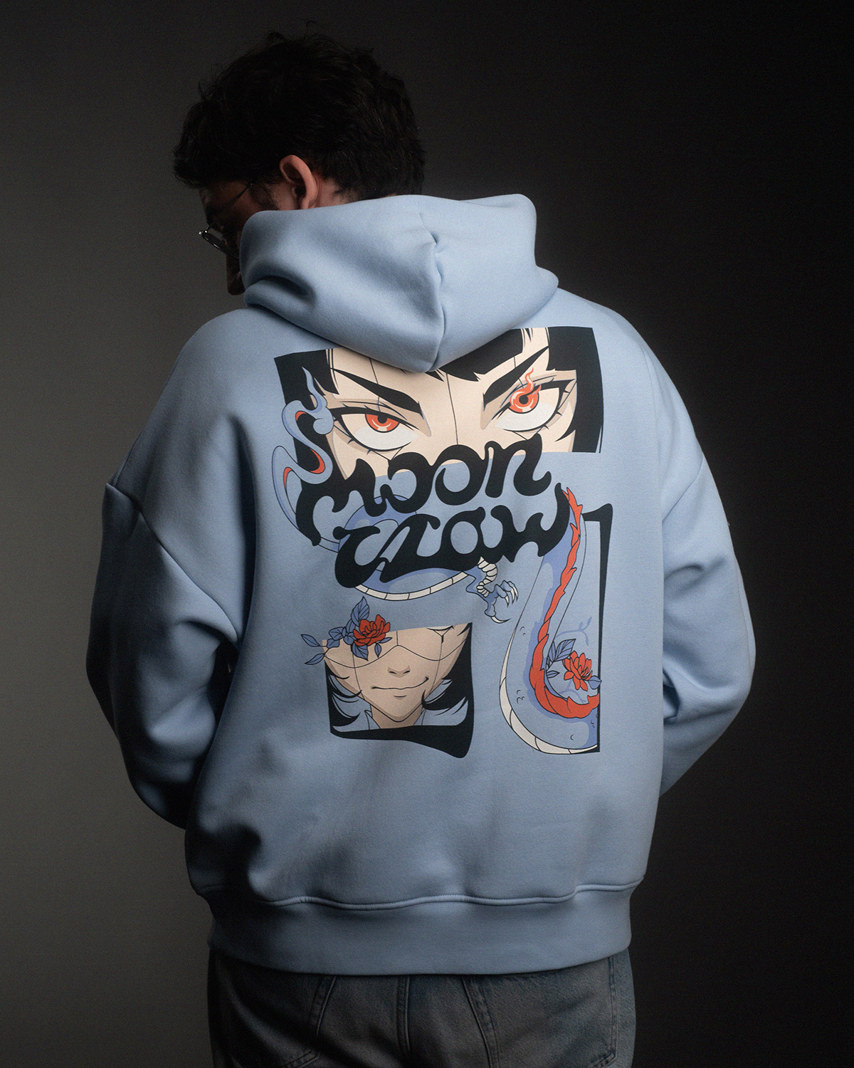 Rückansicht eines hellblauen Hoodies mit großem buntem Print. Das Motiv zeigt ein Paar Augen, eine lächelnde Figur mit Blume und einen flammenartigen Schwanz, ergänzt durch den Schriftzug „moon claw“.