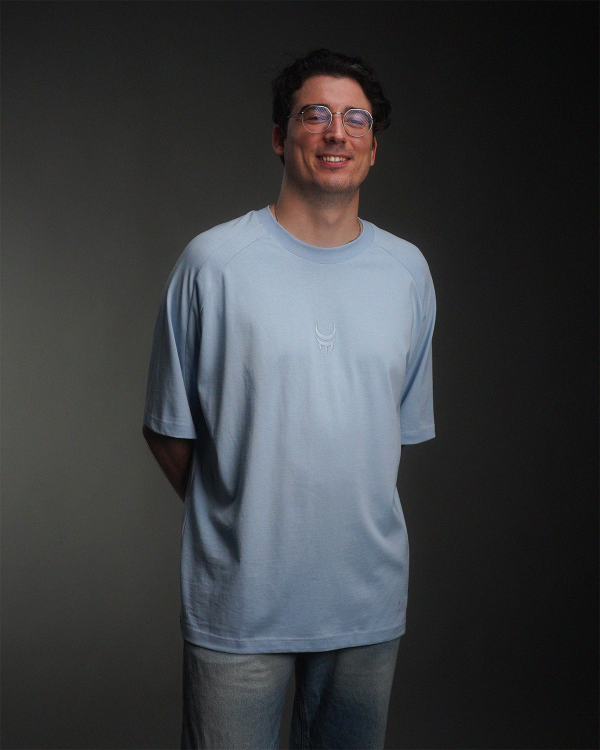 Mann trägt hellblaues T-Shirt mit gesticktem Logo auf der Brust, frontal gezeigt.