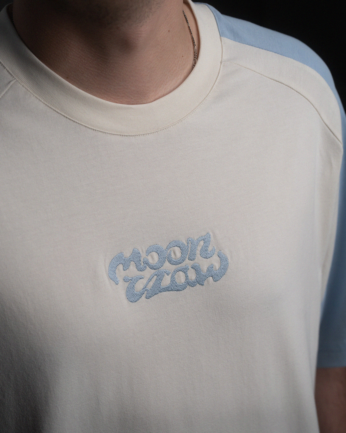 Detailaufnahme der Stickerei auf dem T-Shirt. Der Schriftzug „moonclaw“ erscheint in geschwungener Form in hellem Blau auf der Brust.