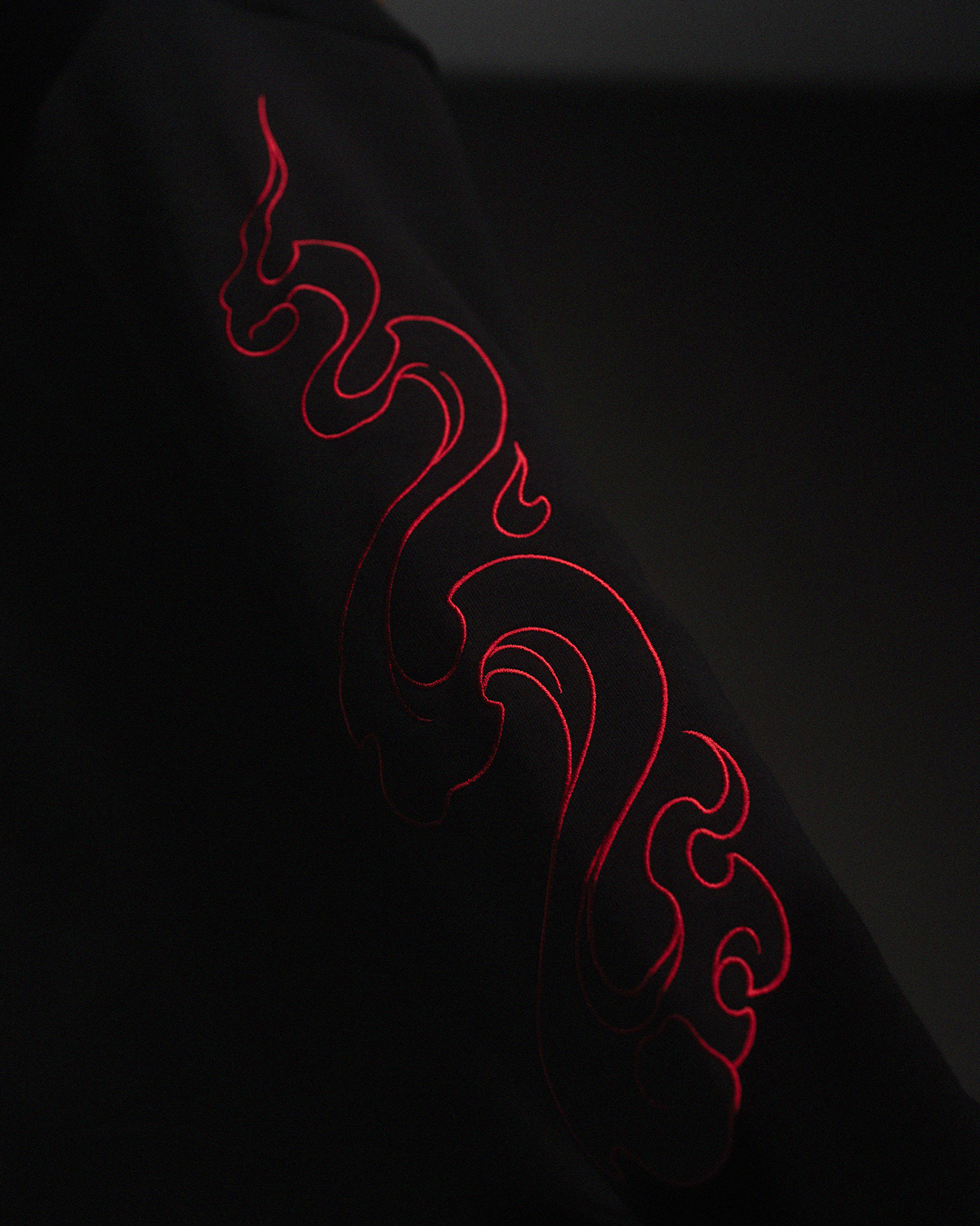 Detailaufnahme eines Ärmels mit auffälliger roter Flammenstickerei auf schwarzem Stoff. Fokus auf Textur und Nahtführung.