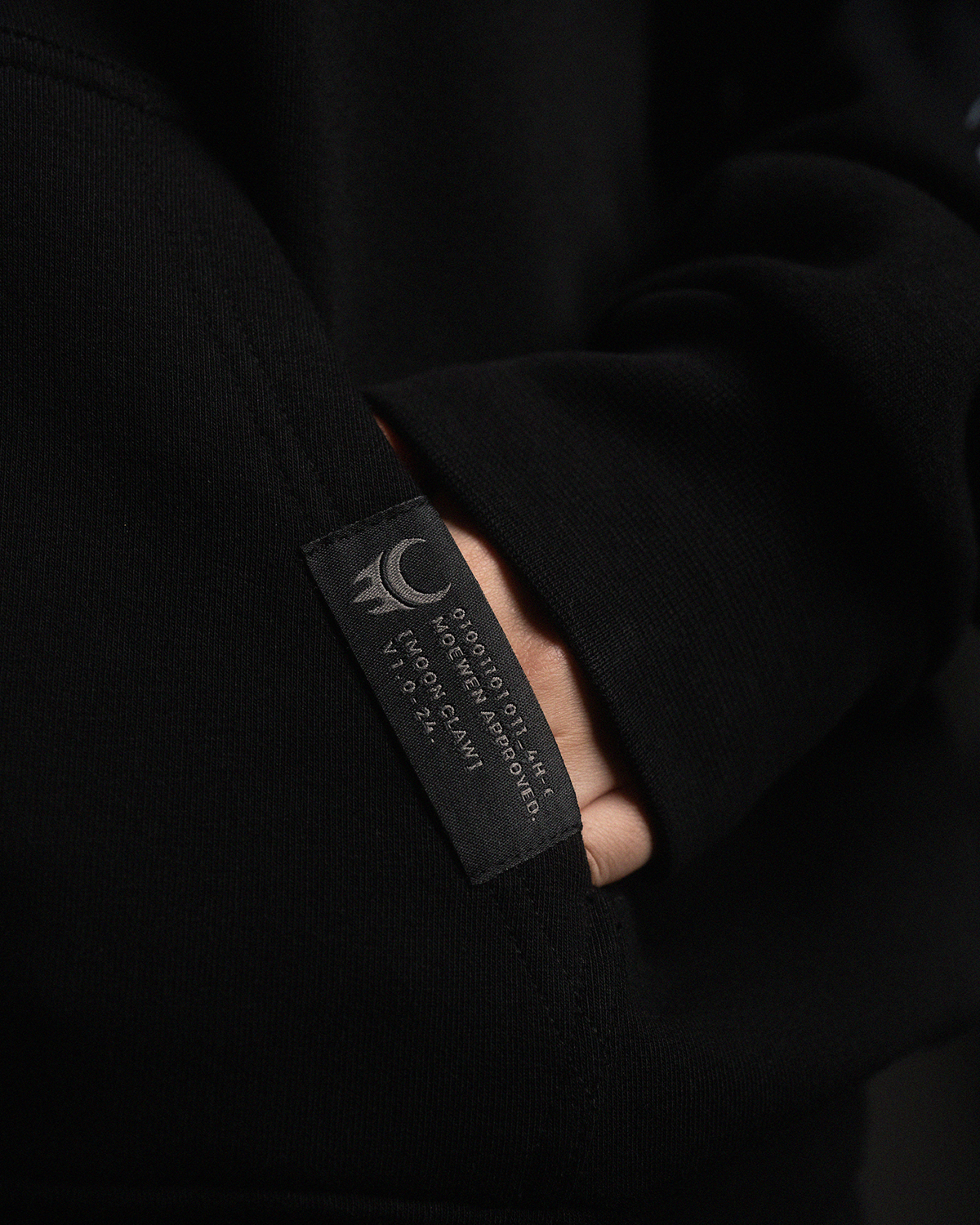 Detailfoto des schwarzen Etiketts an der Kängurutasche der Jacke mit weißem Logo-Print und technischen Angaben.
