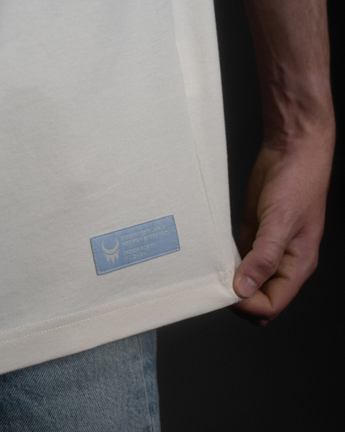 Nahaufnahme eines eingenähten Labels am Saum des Shirts. Hellblaues Label mit Mondkrallen-Symbol und Text „MOON CLAW V1.0.24.“