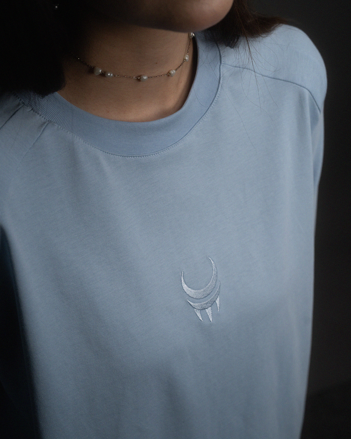 Detailaufnahme des hellblauen Sticklogos auf der Brust eines hellblauen T-Shirts.