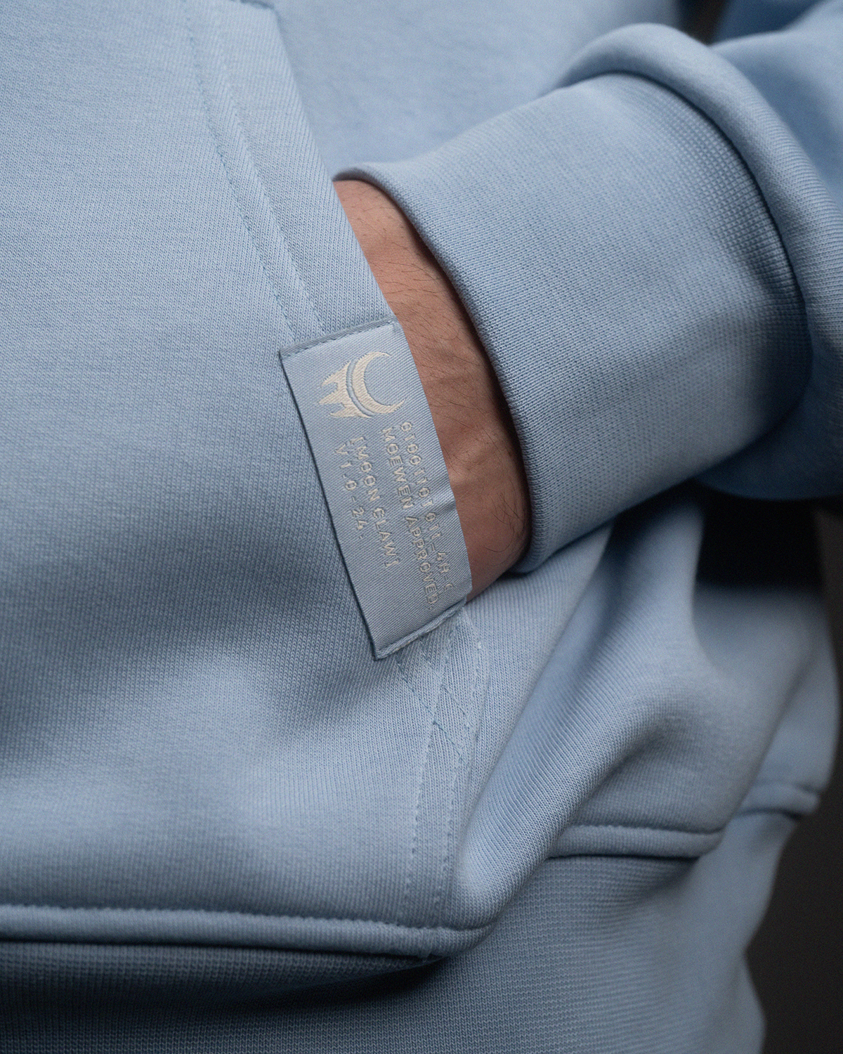Detailaufnahme einer Kängurutasche mit hellem Labelaufnäher am Saum. Das Label trägt das „moon claw“-Logo sowie kleine weiße Schrift.