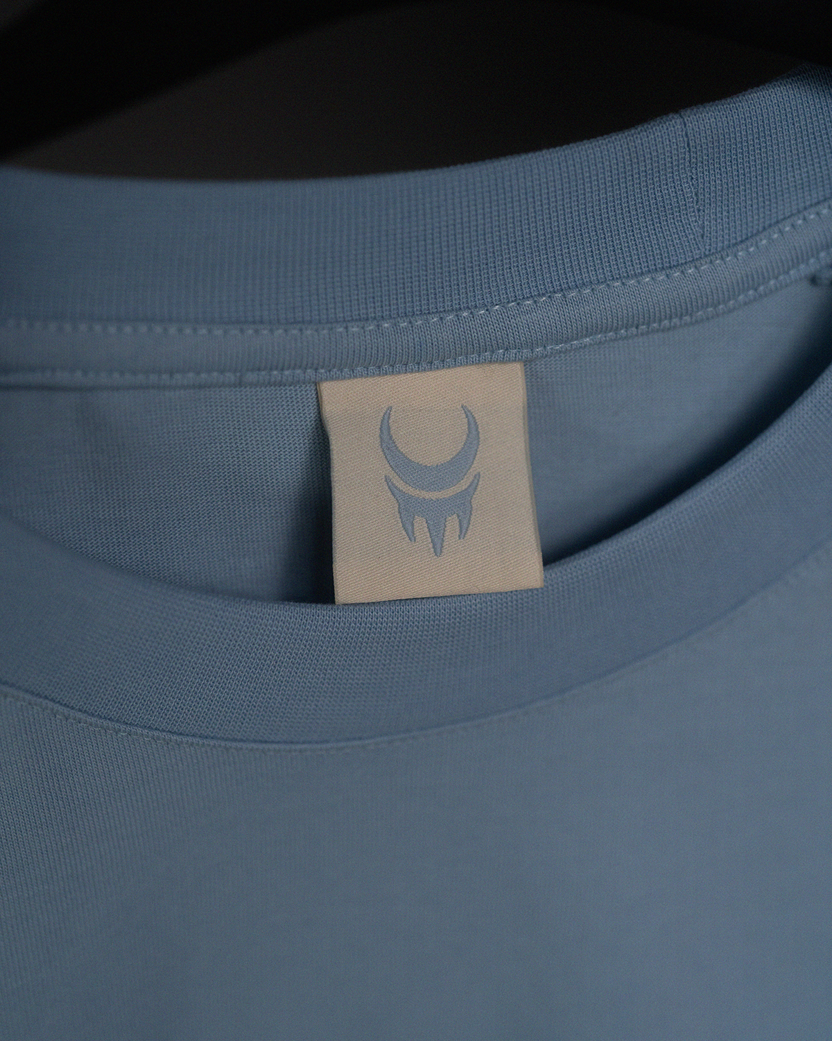 Hellblaues Nackenetikett eines T-Shirts mit stilisiertem Krallensymbol in Hellblau.