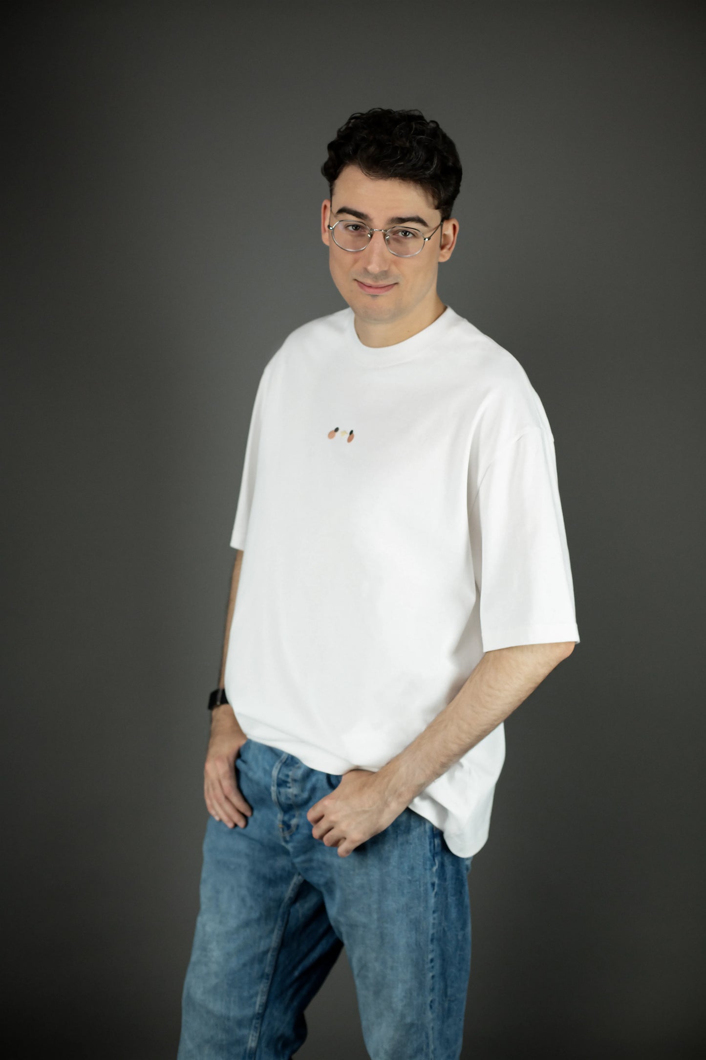 Frontansicht eines weißen Oversized-T-Shirts mit dezentem Stickdetail in der Brustmitte. Das Shirt ist locker geschnitten und wird mit einer hellblauen Jeans kombiniert.